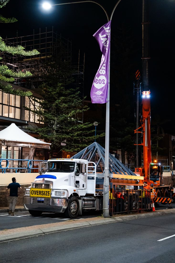 12 tonne rigid truck delivering a steel frame at night beside a crane